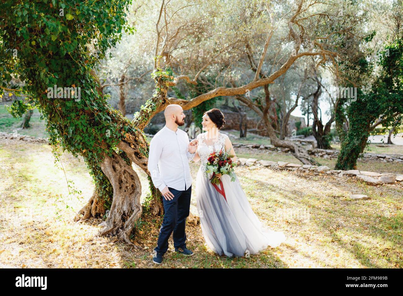 The bride and groom with a bouquet stand hugging among the trees in an ...