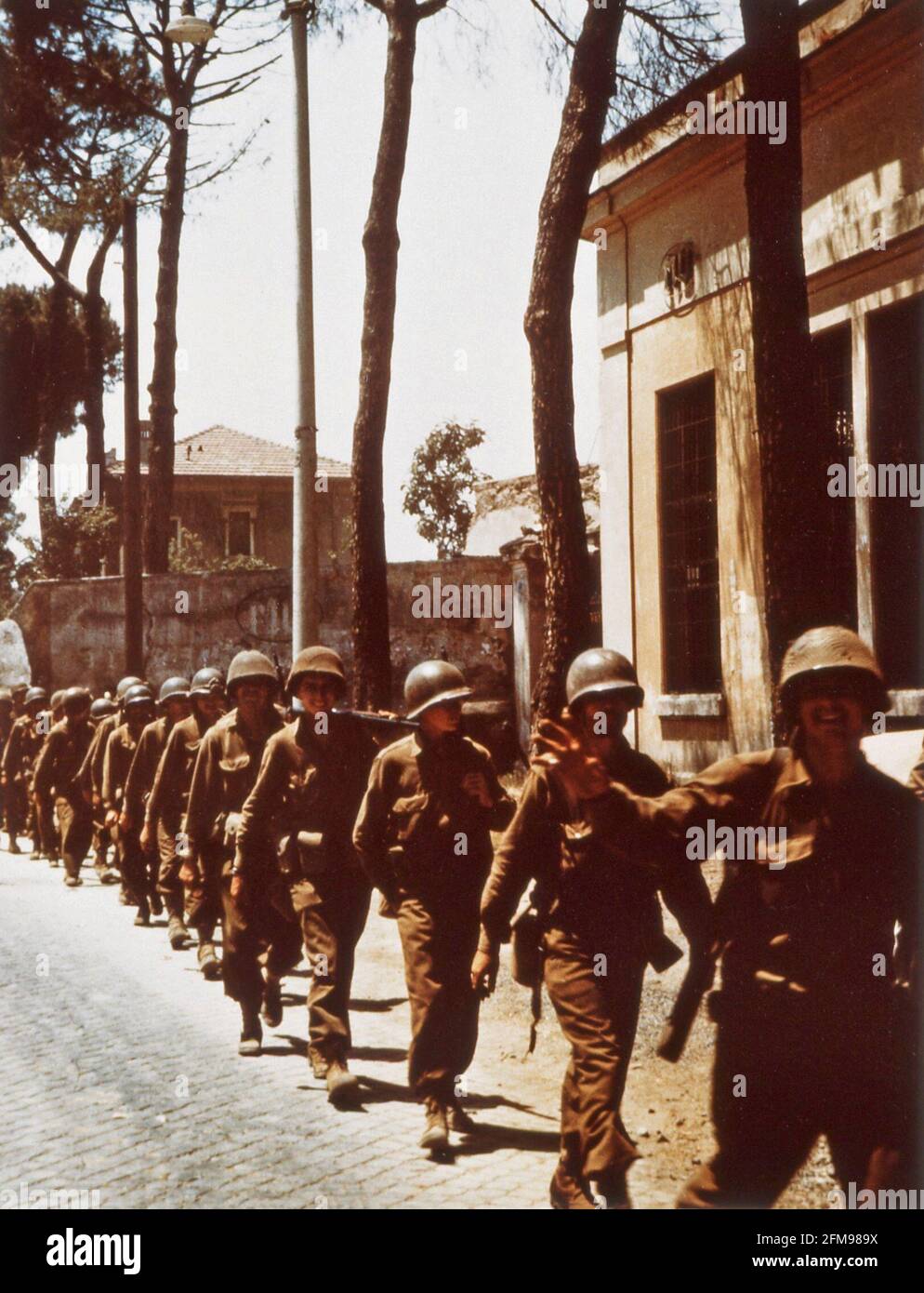 World War Two WWII Color Photo of American army troops walking through an unnamed European town soldier waving Stock Photo