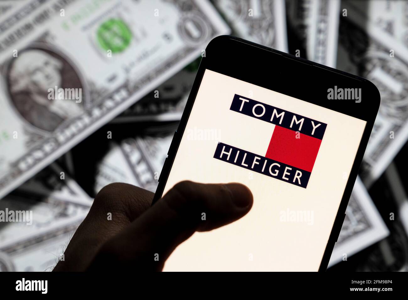In this photo illustration the American fashion brand Tommy Hilfiger logo  seen displayed on a smartphone with USD (United States dollar) currency in  the background Stock Photo - Alamy