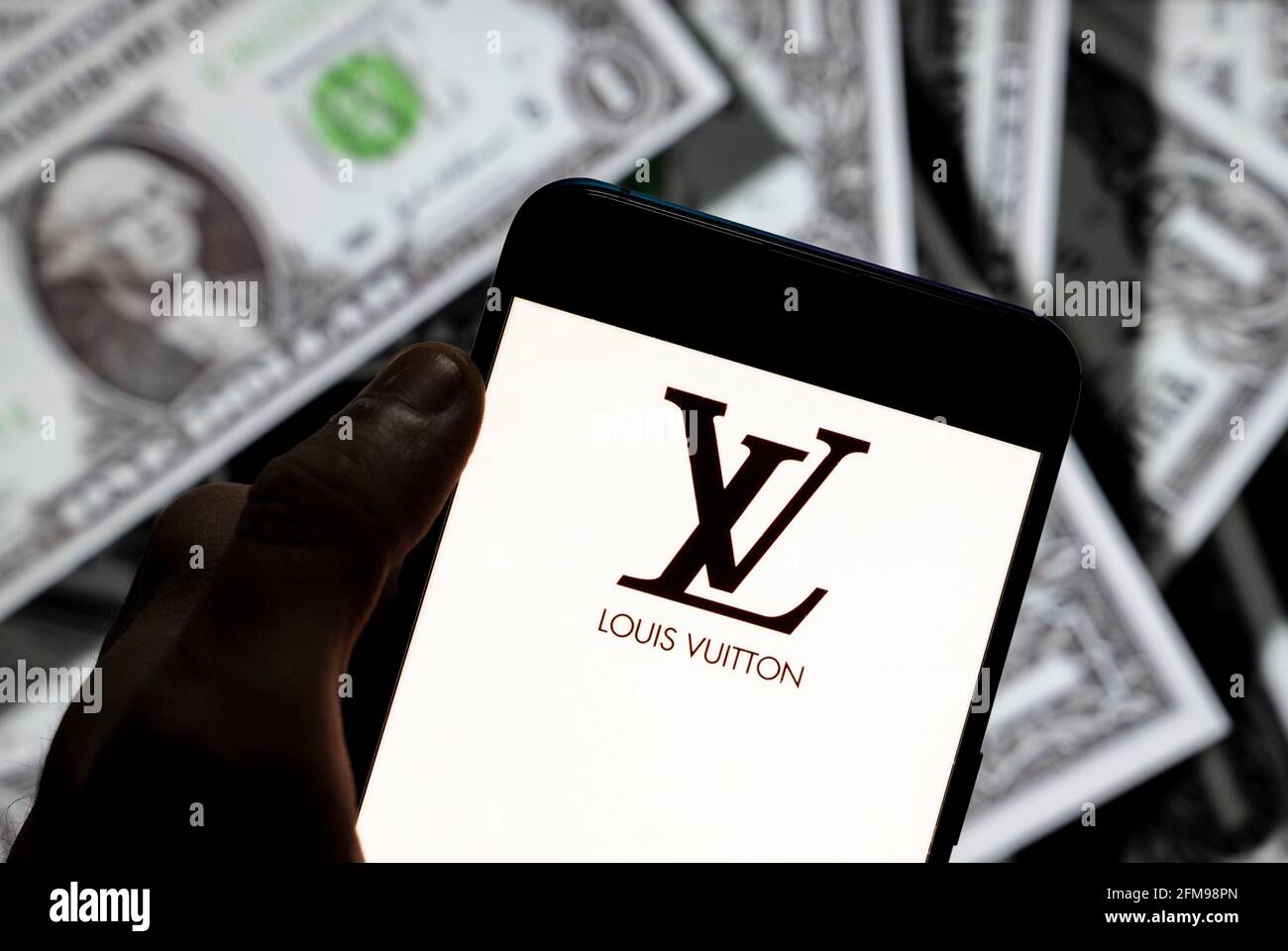 In this photo illustration the French luxury fashion brand Louis Vuitton  logo seen displayed on a smartphone with USD (United States dollar)  currency in the background Stock Photo - Alamy