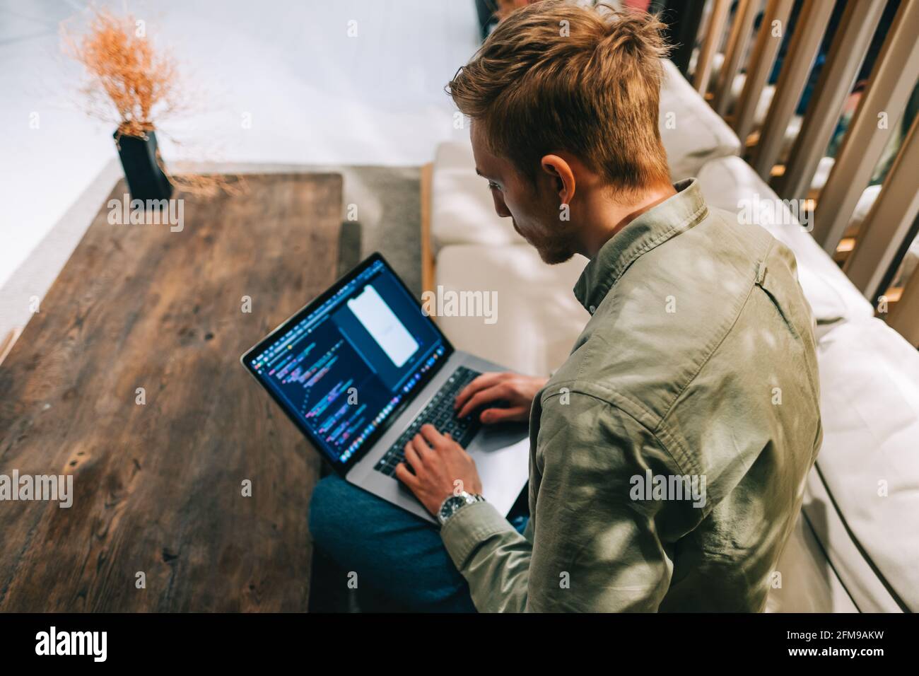 Young man mobile developer with laptop, writes program code on a computer, programmer work in modern office. Stock Photo