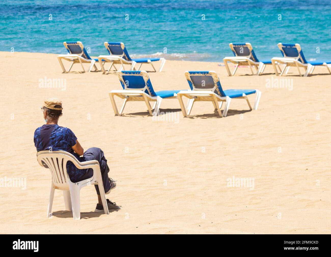Las Palmas, Gran Canaria, Canary Islands, Spain. 7th May, 2021. A man hiring sunloungers waits for customers on a quiet city beach in Las Palmas on Gran Canaria; a popular holiday destination for many British holidaymakers. The beleaguered Canary Islands economy is hoping to be on a list of safe/green places to visit when the UK government makes an  announcement on Friday 7th May. Credit: Alan Dawson/Alamy Live News. Stock Photo