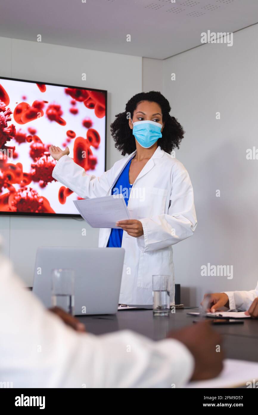 African american female doctor wearing face mask giving presentation to