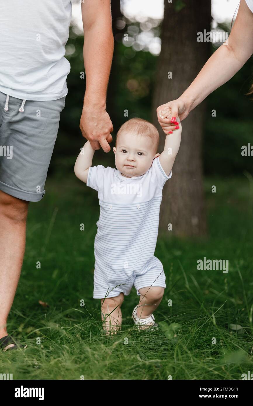 Happy young family, mom, dad and baby son spending time together outdoors  in summer green garden. parents holding their child for hands Stock Photo -  Alamy