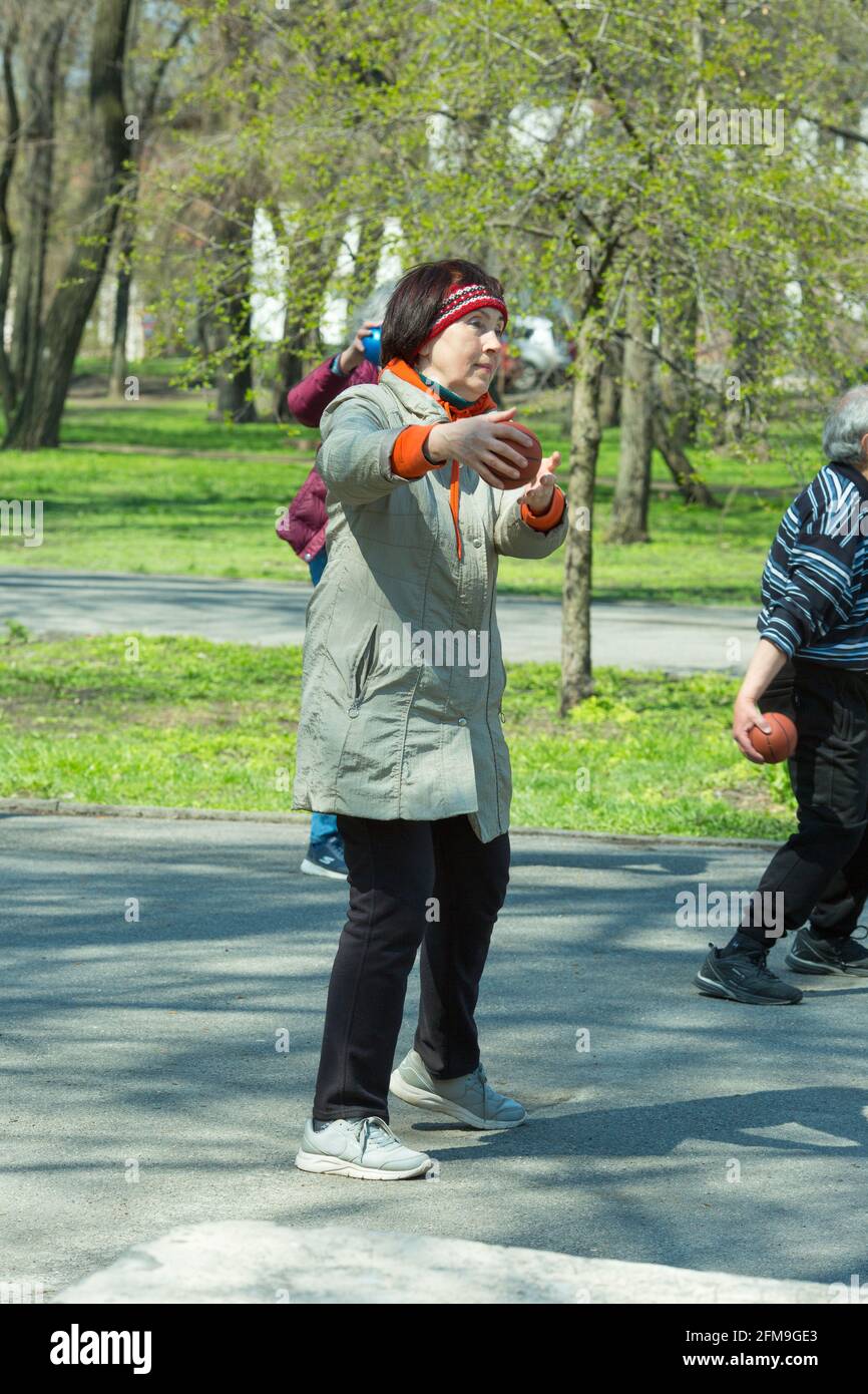 Dnepropetrovsk, Ukraine - 04.22.2021: A group of elderly people doing health and fitness gymnastics in the park. Old people do exercises with a ball. Stock Photo