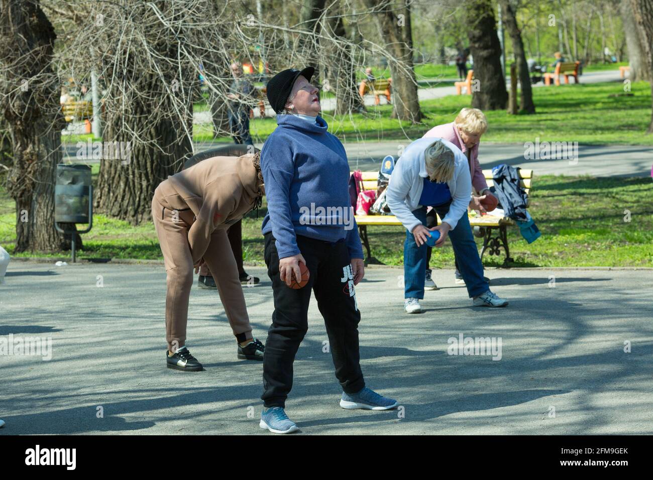Dnepropetrovsk, Ukraine - 04.22.2021: A group of elderly people doing health and fitness gymnastics in the park. Old people do exercises with a ball. Stock Photo