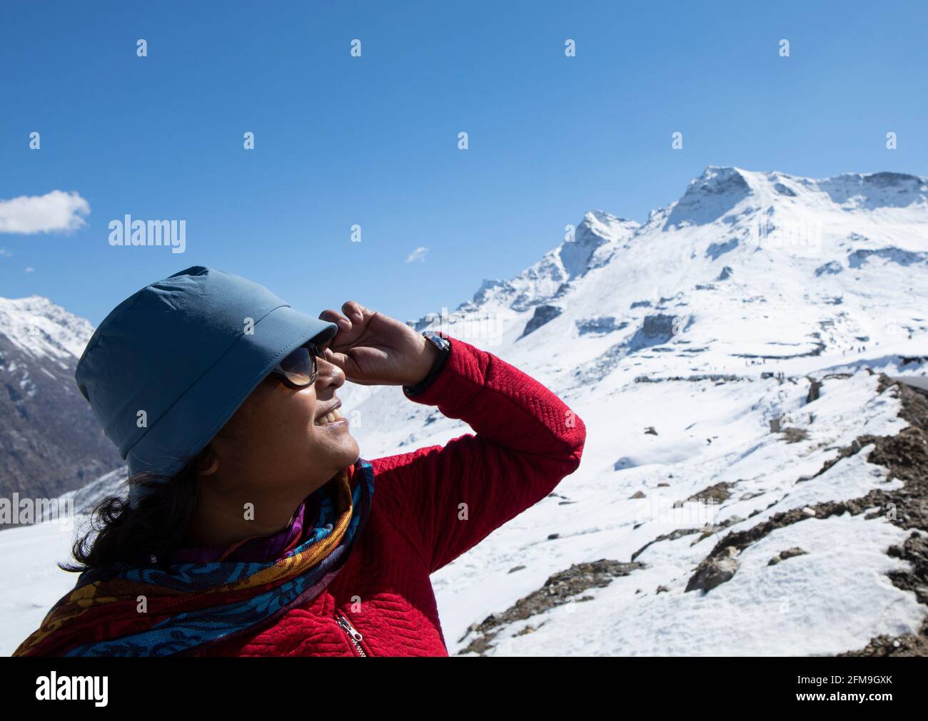 A beautiful young lady with a red sweater, a blue cap and with spectacle enjoying nature on a snow covered high altitude pass on himalaya Stock Photo