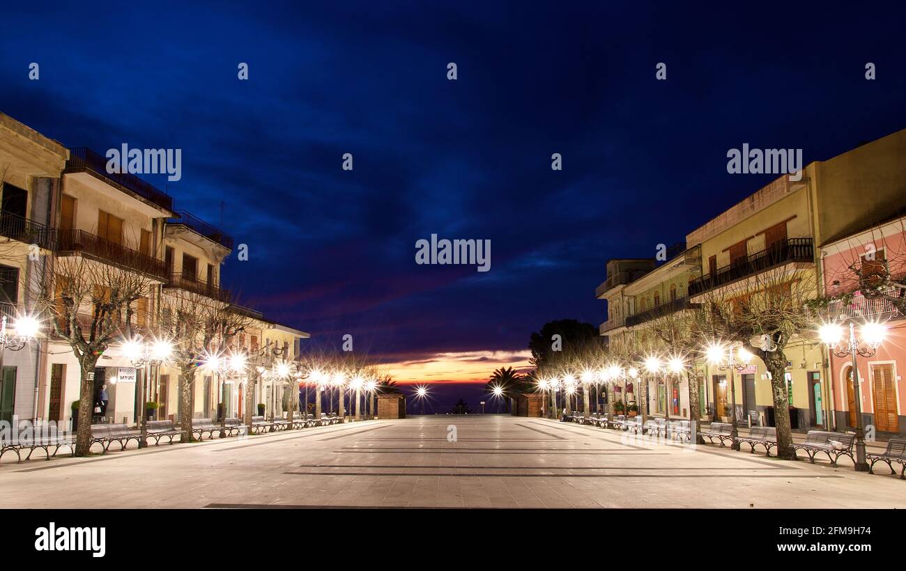 Italy, Sicily, Zafferana Etnea, Piazza Umberto I Belveder, dawn, wider square, left and right lined with street lamps, trees and houses, dark blue night sky, in the background a translucent dawn Stock Photo