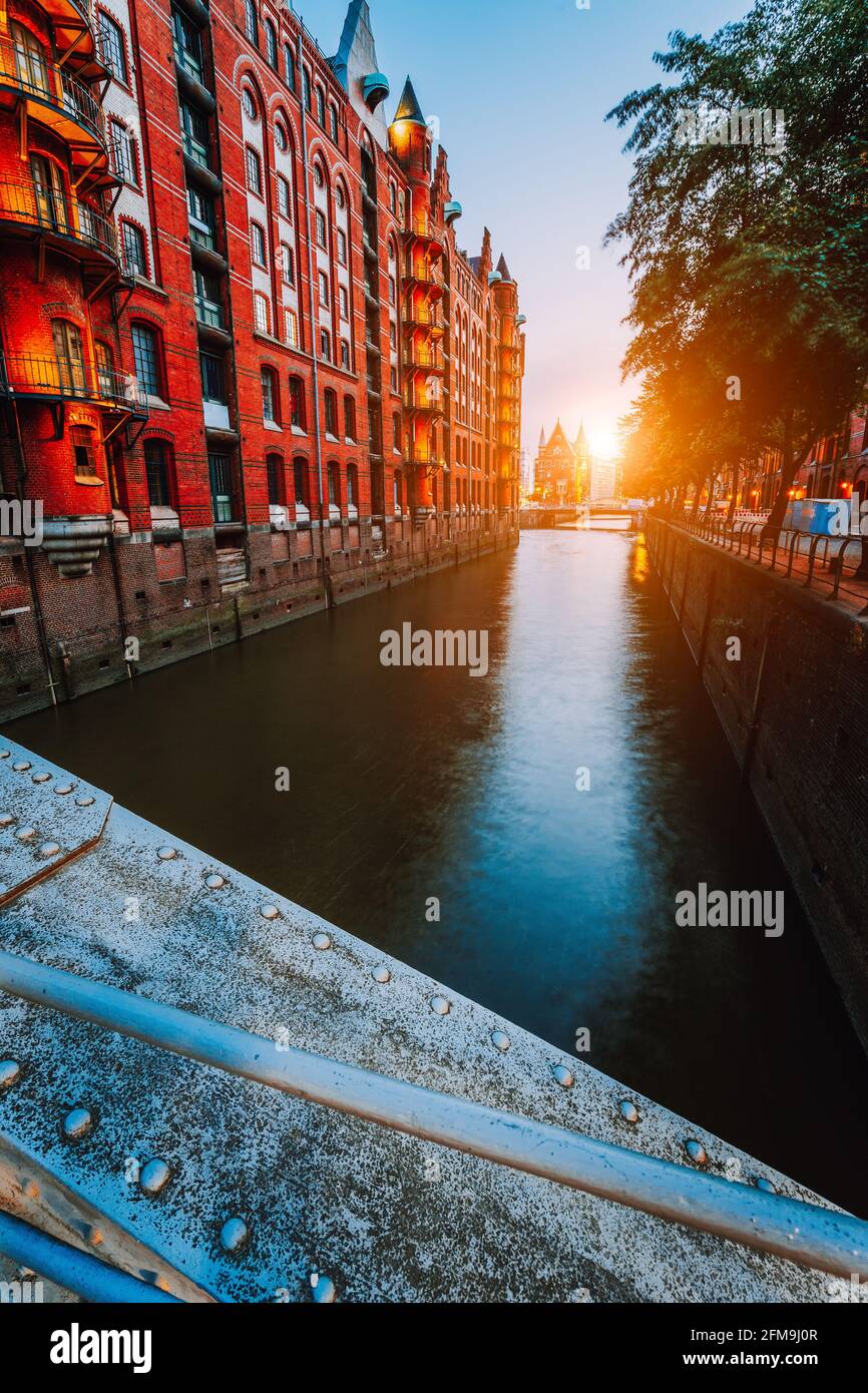 Touristic spot old red brick illuminated buildings, canal and square in golden sunset light. Speicherstadt Hamburg. Warehause District at dawn. Stock Photo