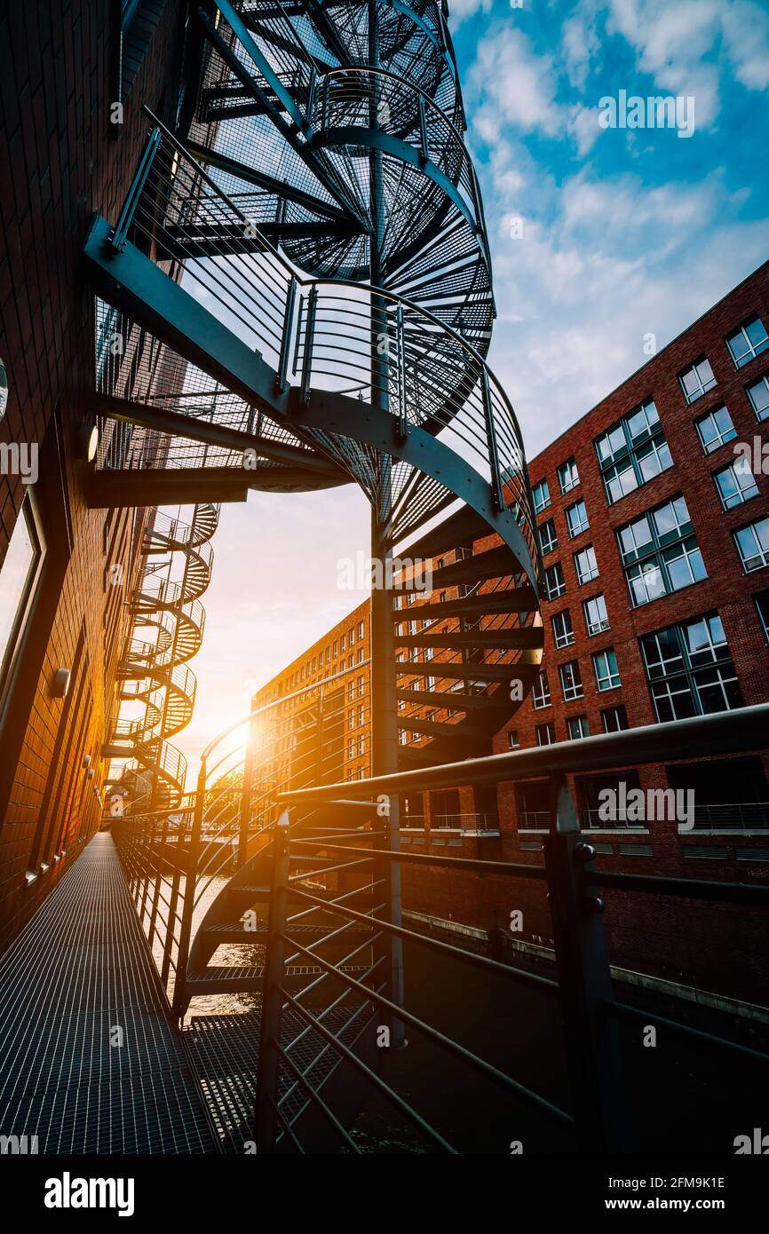 Winding stairs in the old Warehouse District. Narrow canal and red brick buildings of Speicherstadt in Hamburg in the warm sunset light. low angle shot. Stock Photo