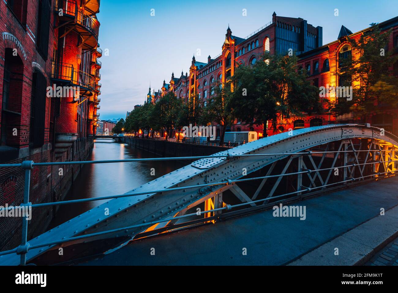 Touristic spot of old bridge and red brick illuminated buildings, canal and square in golden sunset light. Speicherstadt Hamburg. Warehause District at dawn. Stock Photo