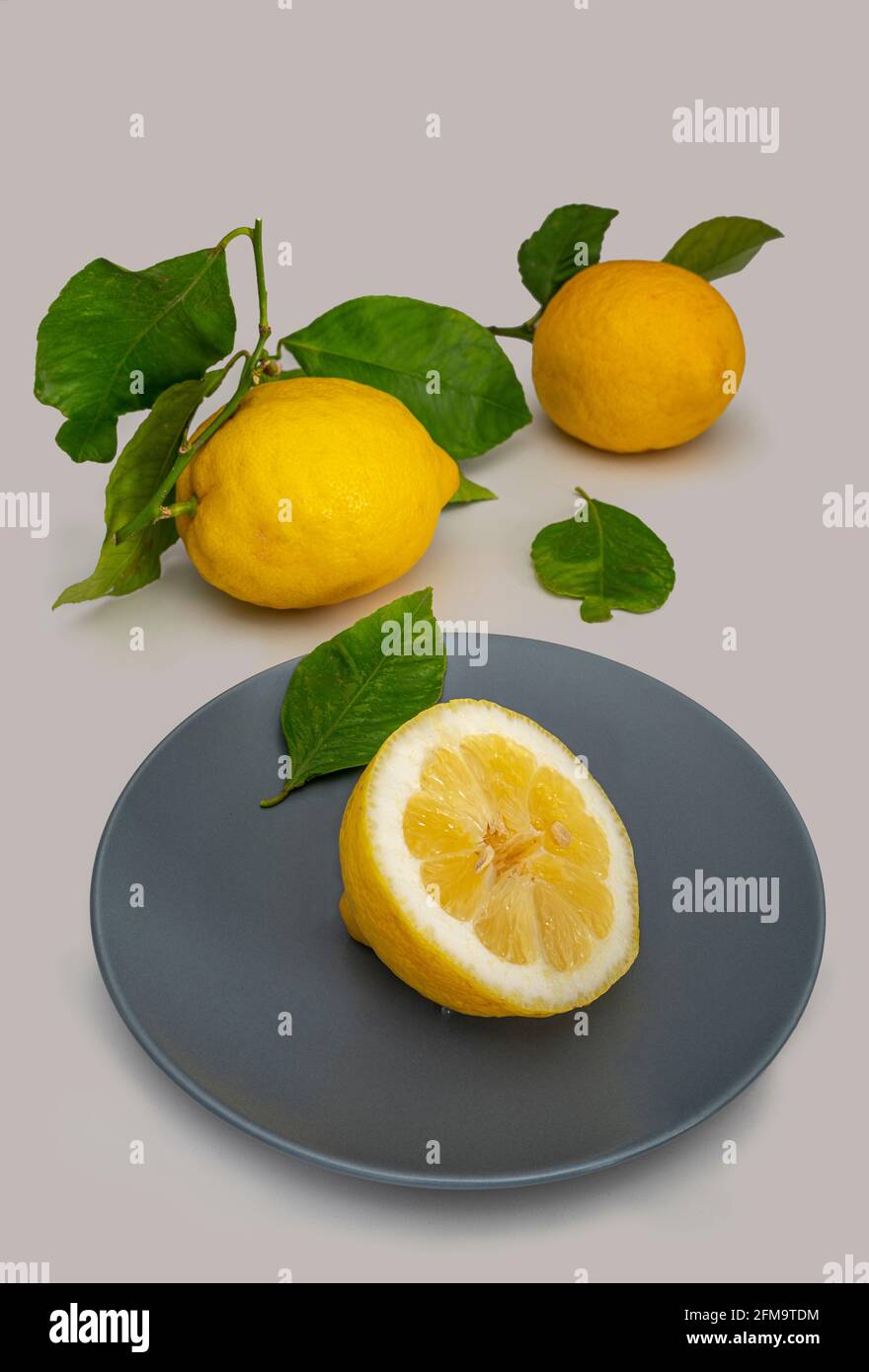 Still life of three lemons one of which is cut in half and placed on a gray plate with the light background. Stock Photo