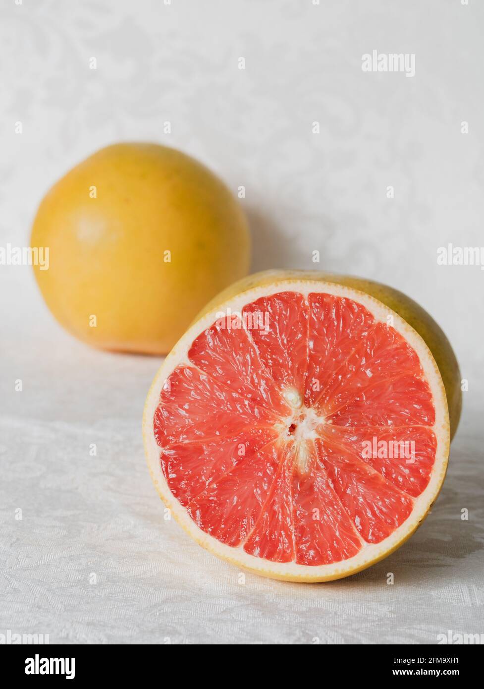 Half a Pink Grapefruit with Whole Grapefruit in Background Stock Photo
