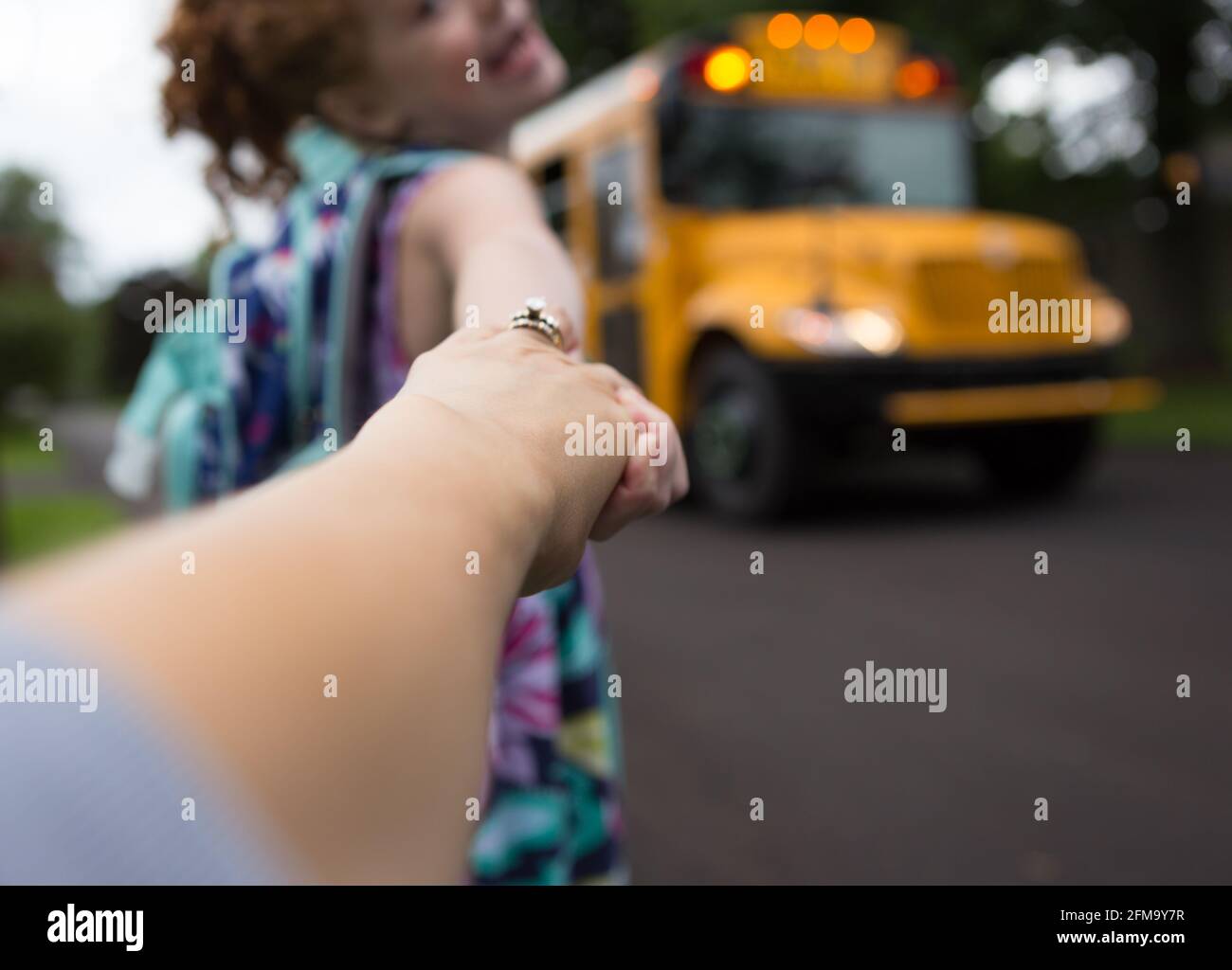 A school age girl holds her mother's hand and smiles back at her while boarding a school bus Stock Photo