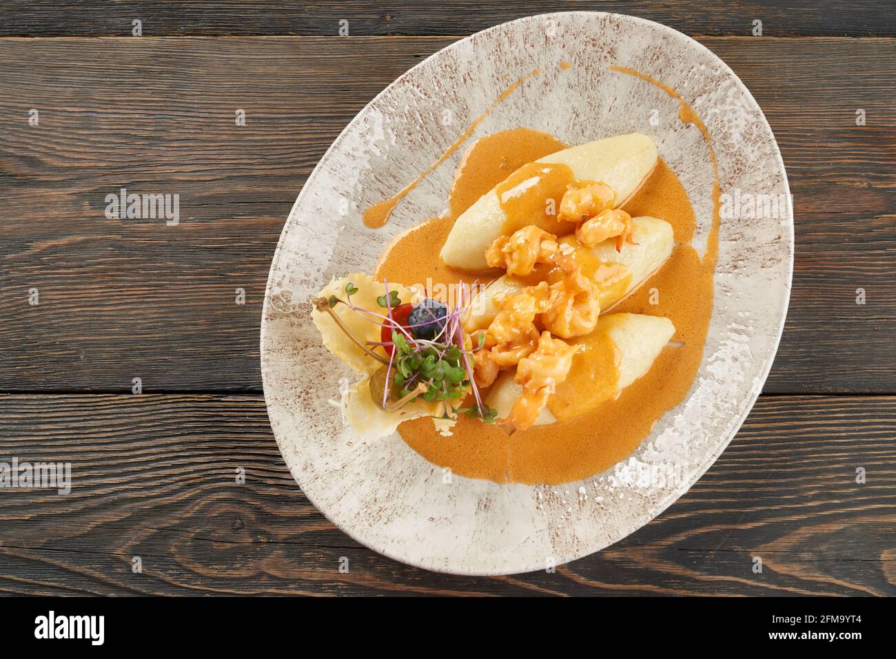 Delicious seafood with orange sauce on plate on table, three potato cutlets served with vegetables and sprouts. From above view of shrimps cooked in restaurant for dinner. Concept of food and cuisine. Stock Photo