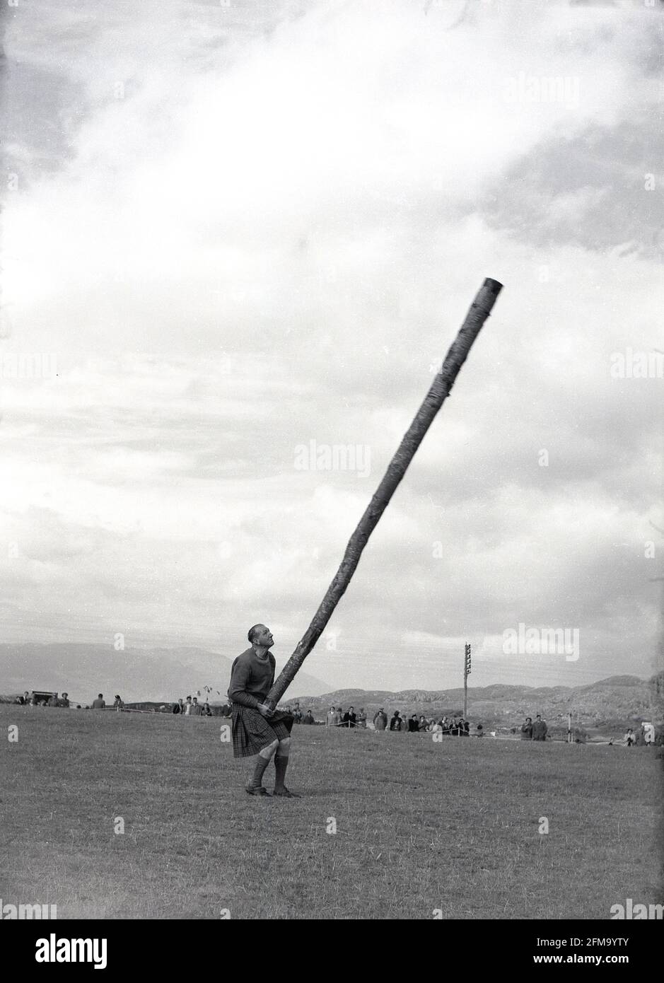 1956, a male competitor at a highland games about to toss the caber, Scotland, A traditional and well-loved athletic event at a Scottish highland games, the 'caber toss' involves a competitor tossing a long, heavy pole so that it turns end over end. Usually made from a Larch tree, and up to 20 feet in length, the caber is stood upright and then lifted up and tossed, not thrown. Caber is the Gaelic word for pole. Devised by Scottish woodsmen, the caber toss was first recorded in 1574, at a military meet  as toss 'ye barr', when clan warriors tested their physical strength in sporting contests. Stock Photo