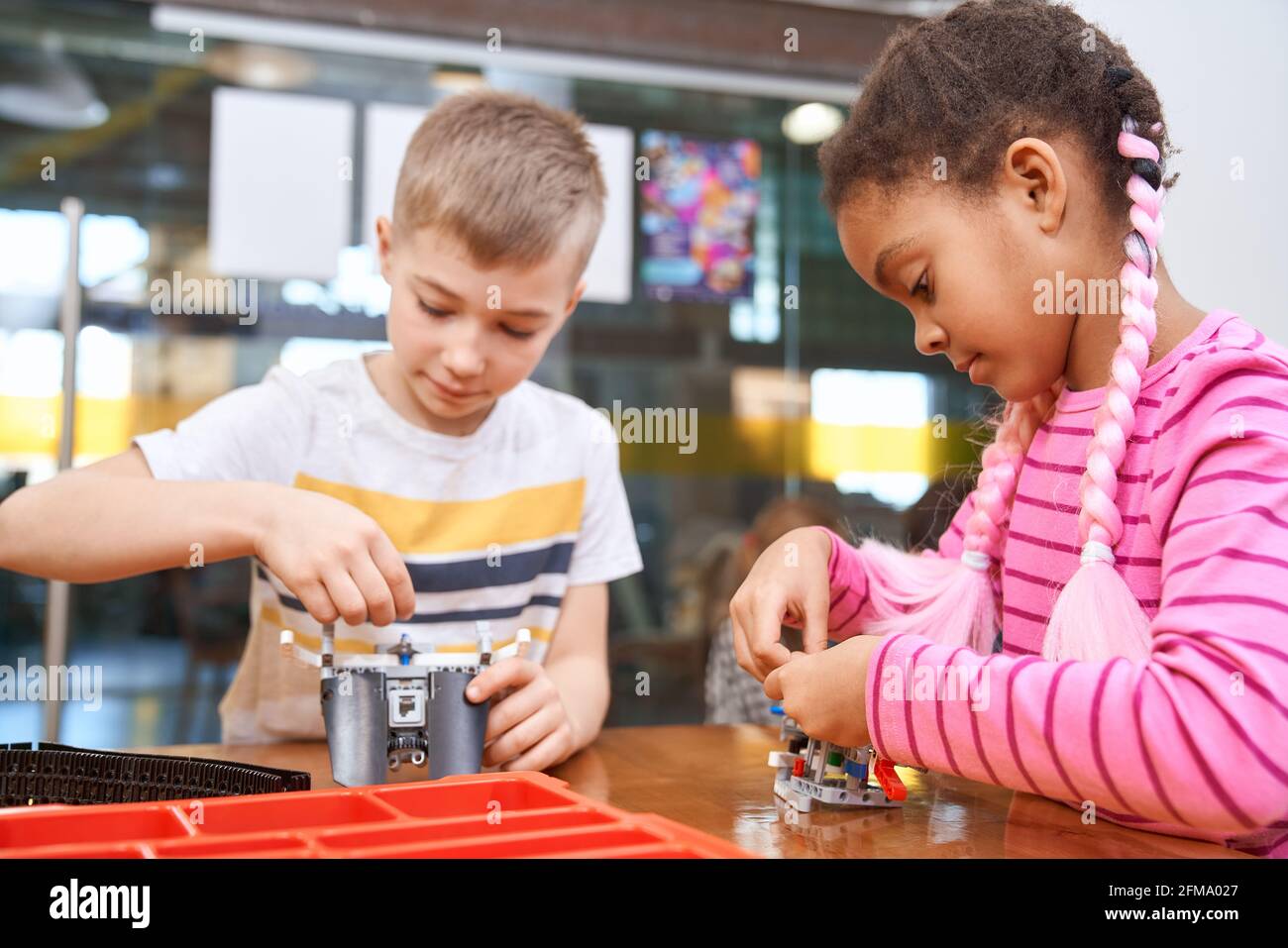 Building kit for group of multiracial kids creating toys. Close up of concentrated african girl and caucasian boy working on project, having positive emotions. Concept of science engineering. Stock Photo