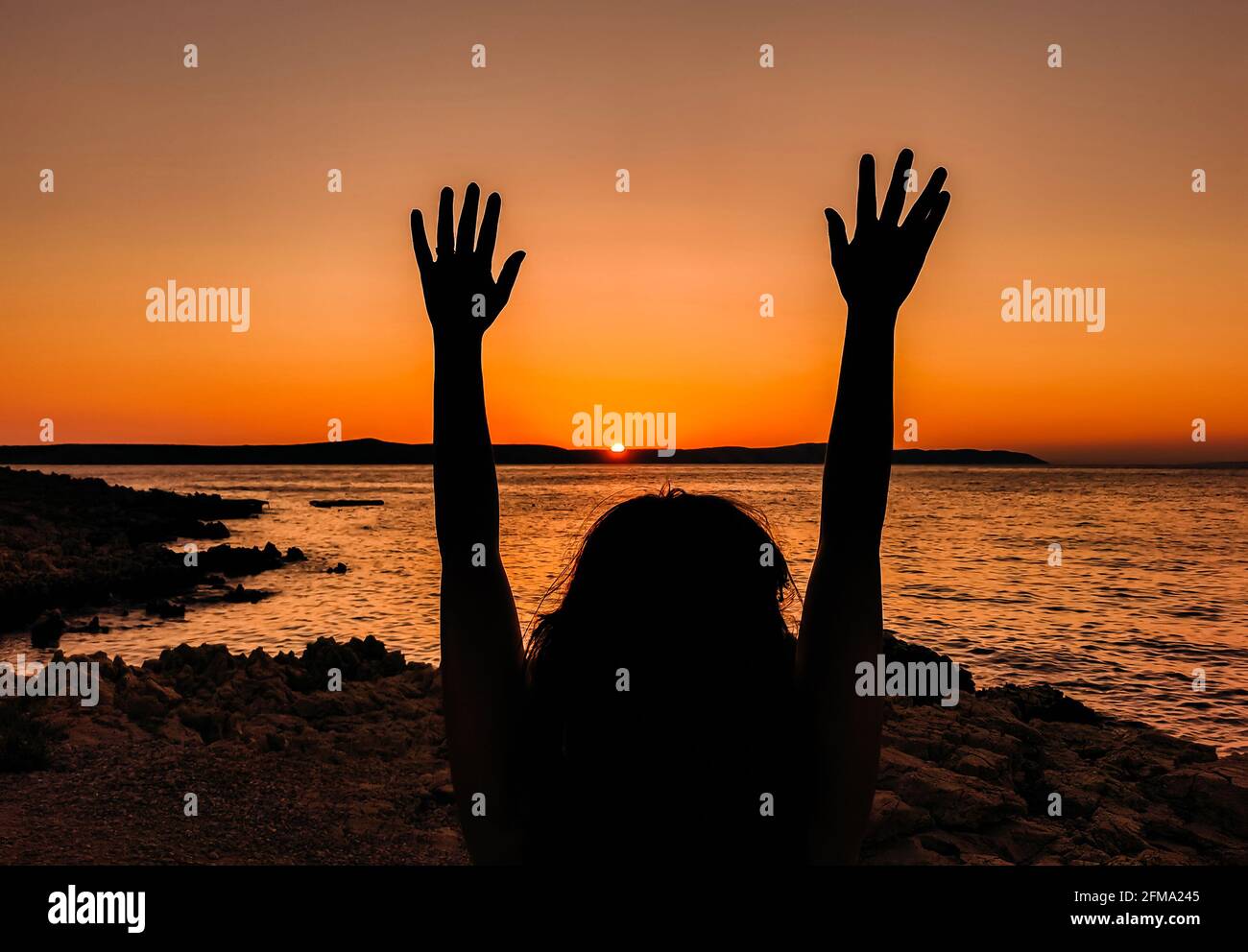Silhouette of woman with raised arms standing on sea shore, looking at ...
