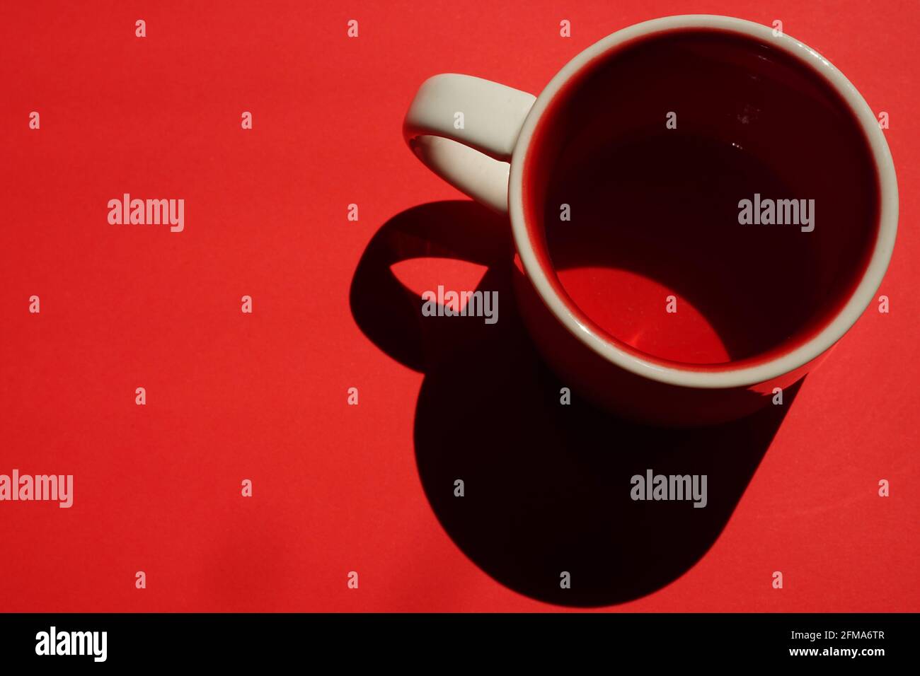 Beige cup with red inside on a red table. Light and shadow. Top view. Copy space Stock Photo
