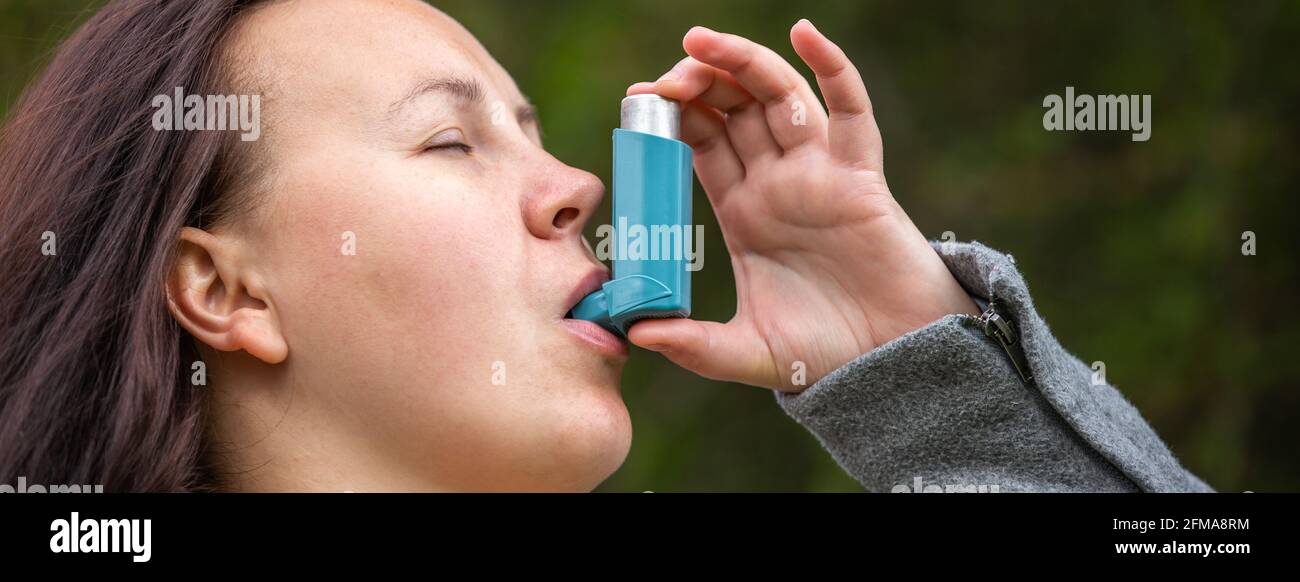 Pretty young brunette woman using asthma inhaler during strong asthma attack, pharmaceutical product is used to prevent and treat wheezing and Stock Photo