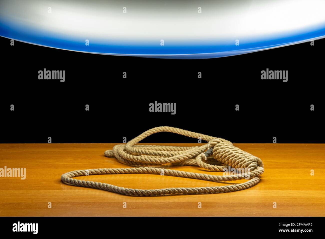 A noose lying on the table under a light of moving chandelier, on a black background Stock Photo