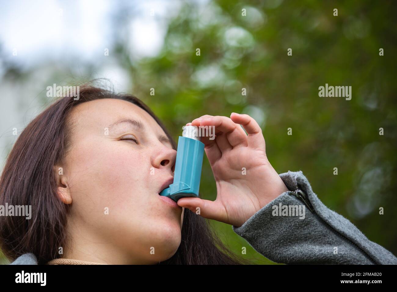 Pretty young brunette woman using an asthma inhaler during strong asthma attack, pharmaceutical product is used to prevent and treat wheezing and Stock Photo