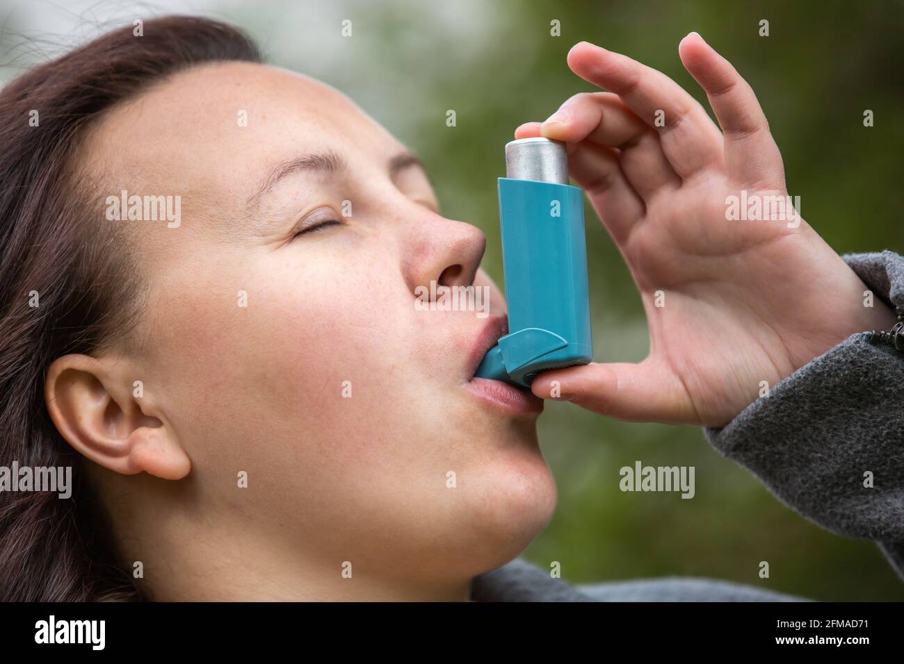 Pretty young brunette woman using asthma inhaler during strong asthma attack, pharmaceutical product is used to prevent and treat wheezing and Stock Photo