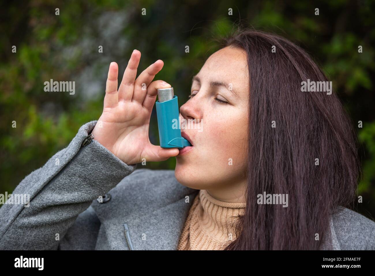 Pretty young brunette woman using an asthma inhaler during strong asthma attack, pharmaceutical product is used to prevent and treat wheezing and Stock Photo