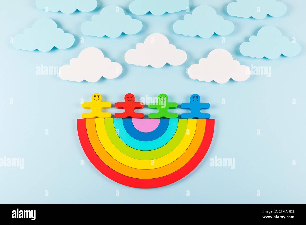 International Children's Day background. Wooden toy children with the rainbow on the light blue background. Flat lay. Copy space. Stock Photo