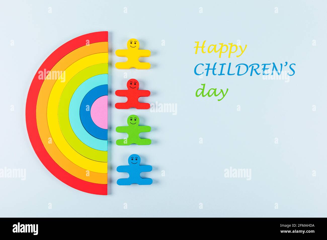 International Children's Day background. Wooden toy children with the rainbow on the light blue background. Flat lay. Copy space. Stock Photo