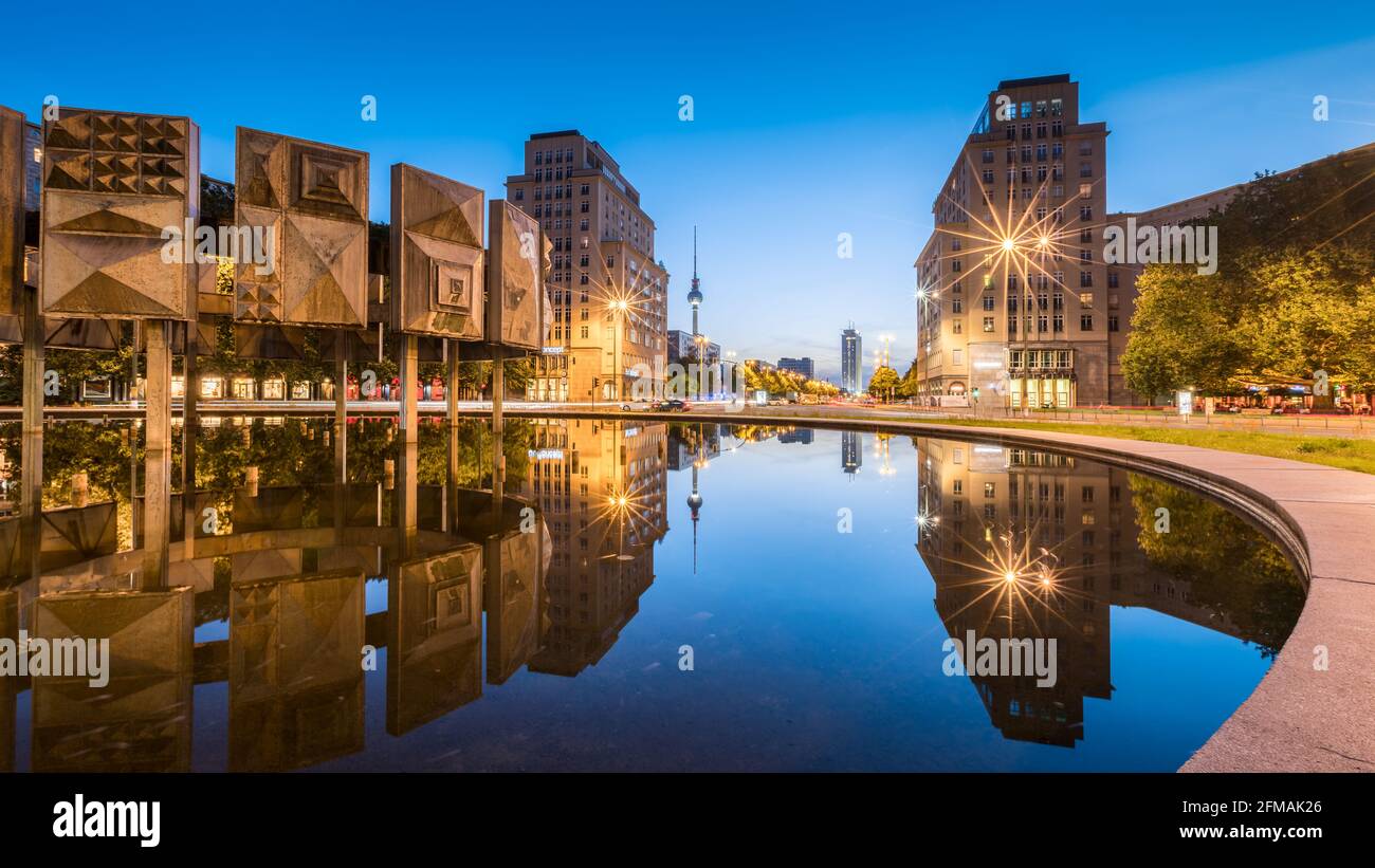 Reflection of the buildings on Strausberger Platz in the water of the fountain with the television tower in the background at the blue hour. Stock Photo