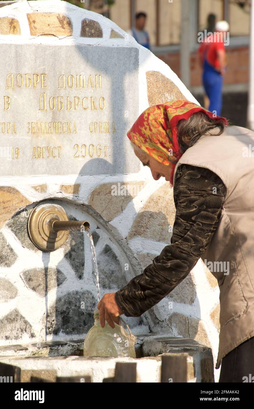 Bulgarian woman collecting water in the street, Gorno Draglishte. Razlog Municipality, Blagoevgrad province, Bulgaria Stock Photo