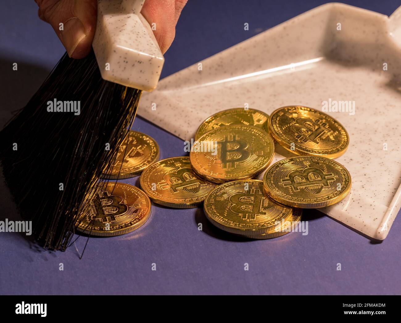 Brushing bitcoins into a dustpan as concept for the collapse in value of cyber coins and digital currency Stock Photo