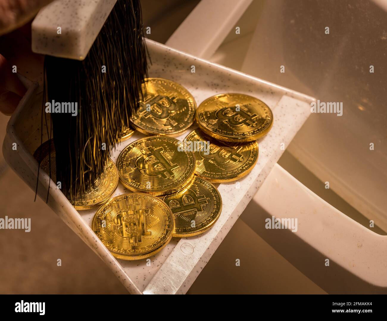 Brushing bitcoins into a dustpan as concept for the collapse in value of cyber coins and digital currency Stock Photo