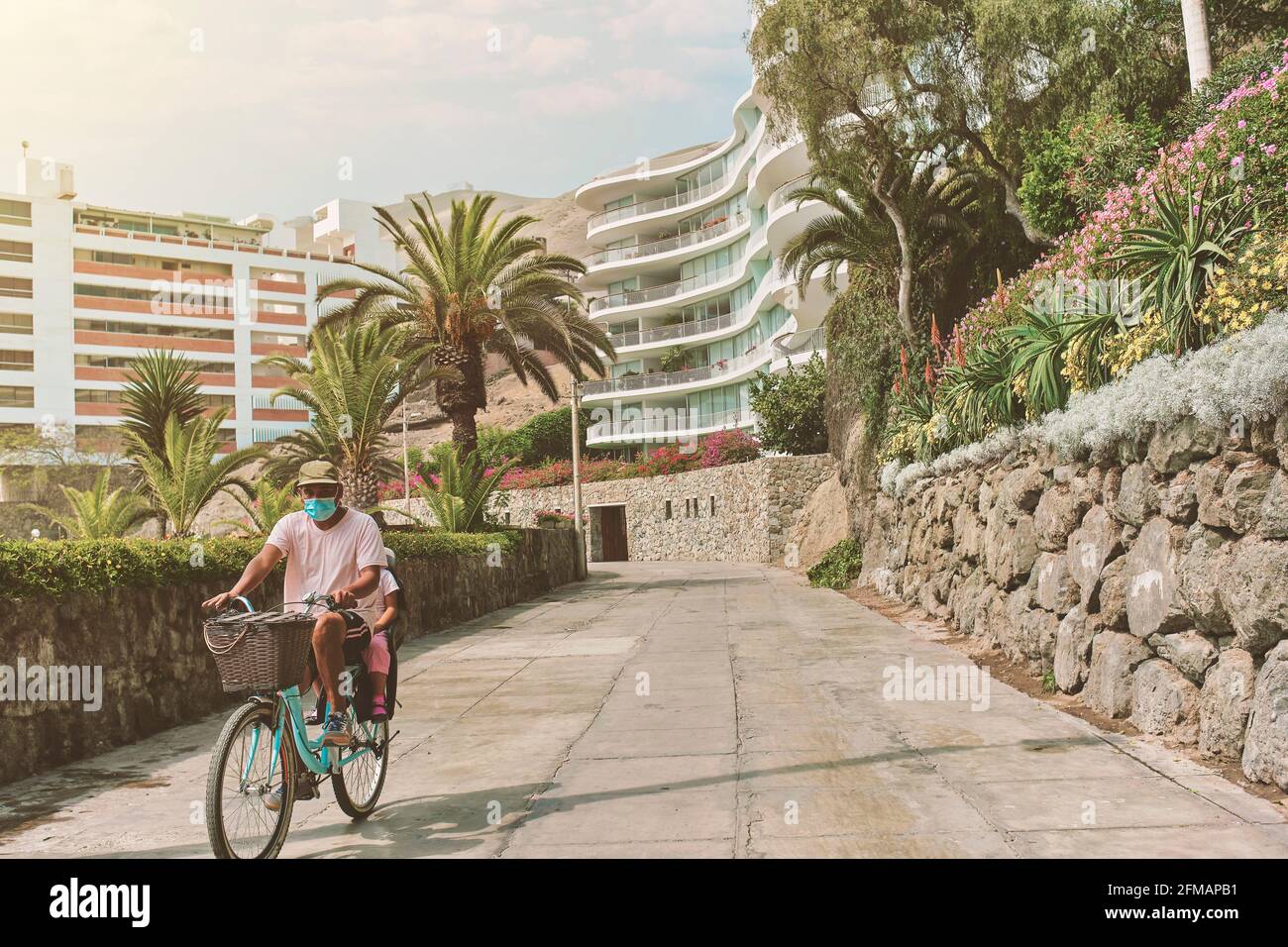 Father with mask on bicycle with his son in a baby seat, morning walk on the boulevard, sunny day. New normal concept Stock Photo