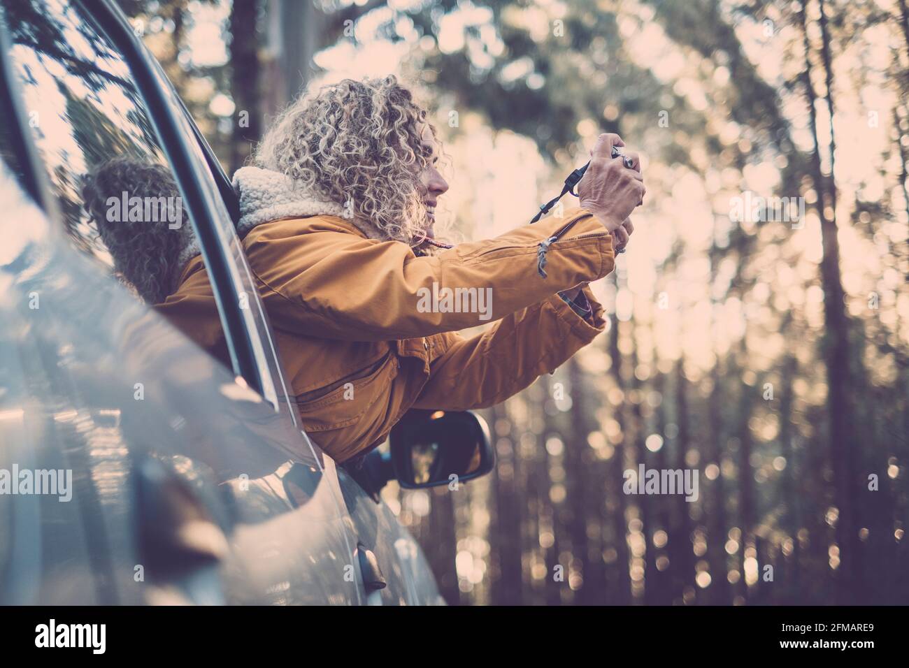 adventure vacation, holidays, travel, road trip and people concept - happy smiling young adult woman or young woman outside the car window taking picture to the forest woods nature Stock Photo