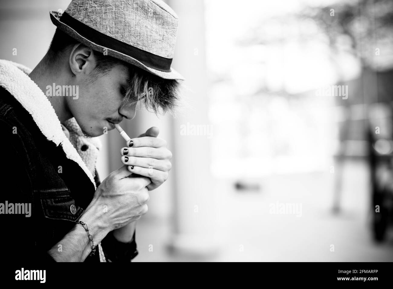 Black and white young boy teenager portrait lighting a cigarette to smoke in youth age - un healthy lifestyle - cool alternative caucasian hispanic guy lifestyle Stock Photo