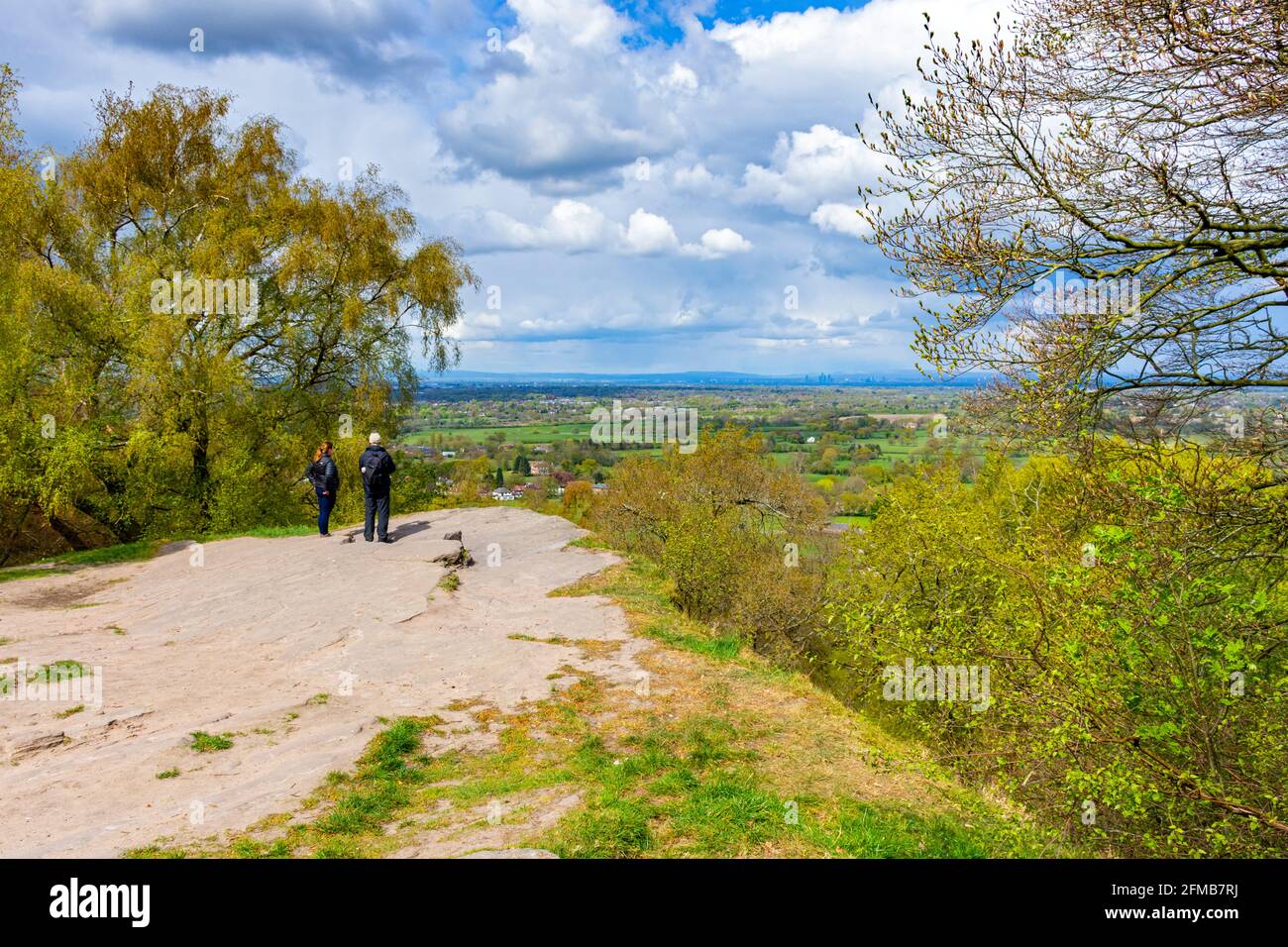 A couple looking out over the Cheshire Plain to the distant towers of Manchester city centre.  From Alderley Edge, Cheshire, England, UK. Stock Photo