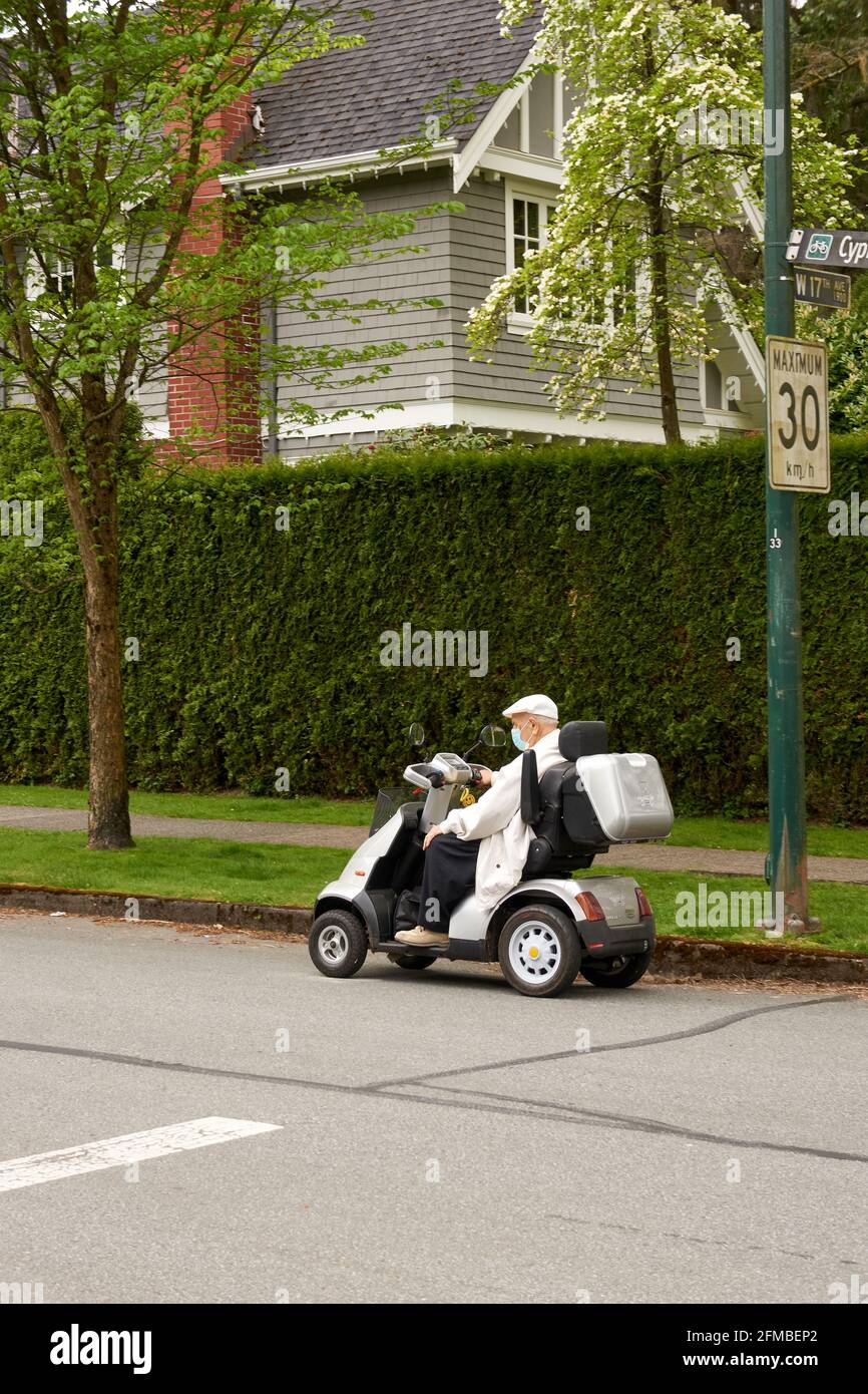 Elderly man riding an electric mobility scooter on a residential street Stock Photo