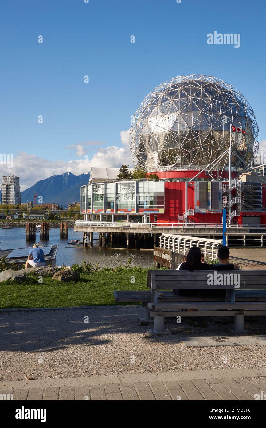 People relaxing on the waterside walkway with the Telus World of Science geodesic dome in background, Village on False Creek, Vanouver, BC, Canada Stock Photo