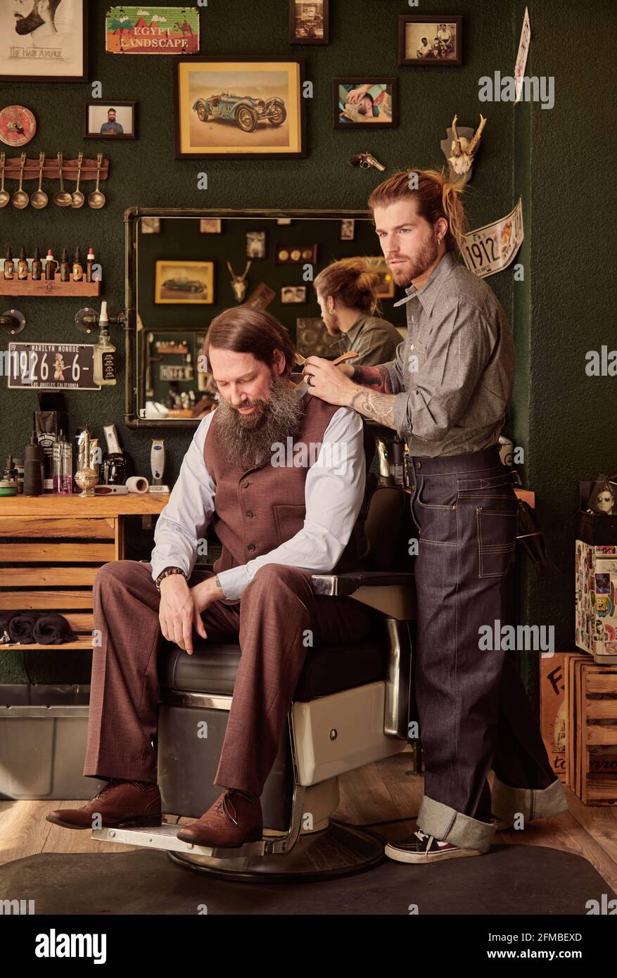Young man coiffures bearded man in barbershop Stock Photo