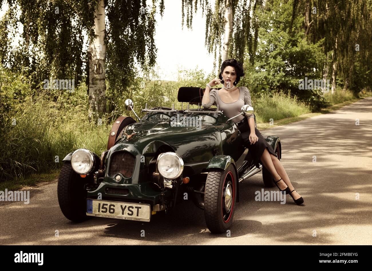 Young 1940s style woman with vintage car in British Racing Green Stock Photo