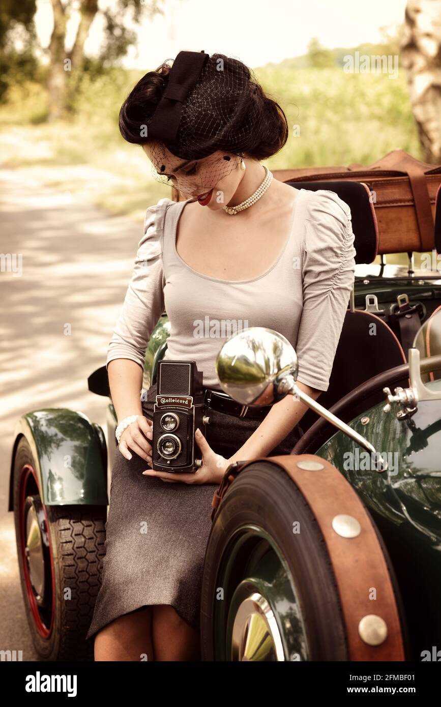 Young 1940s style woman with vintage car in British racing green and old camera Stock Photo