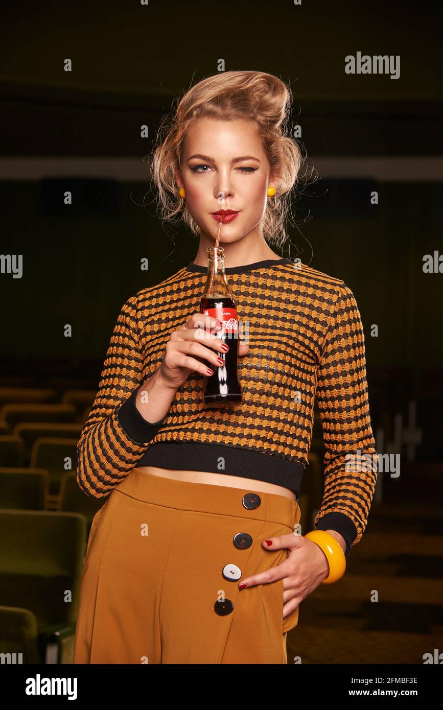 Retro style young blonde woman with coke bottle in cinema room Stock Photo