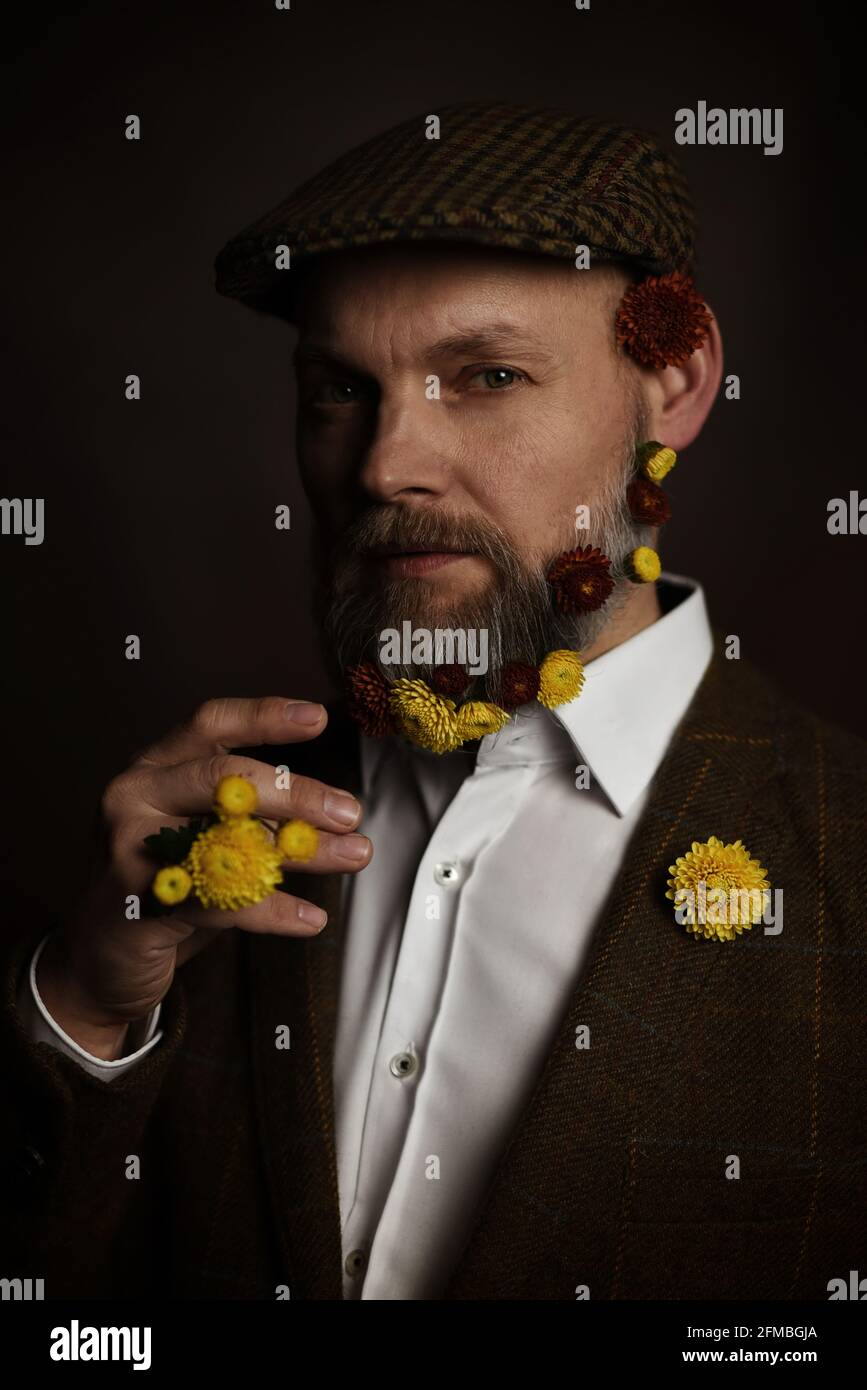 Man in a flat cap with flowers in his beard Stock Photo