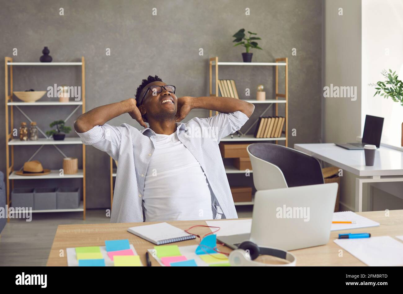 Happy smiling african american businessman with hands behind head sit at desk Stock Photo