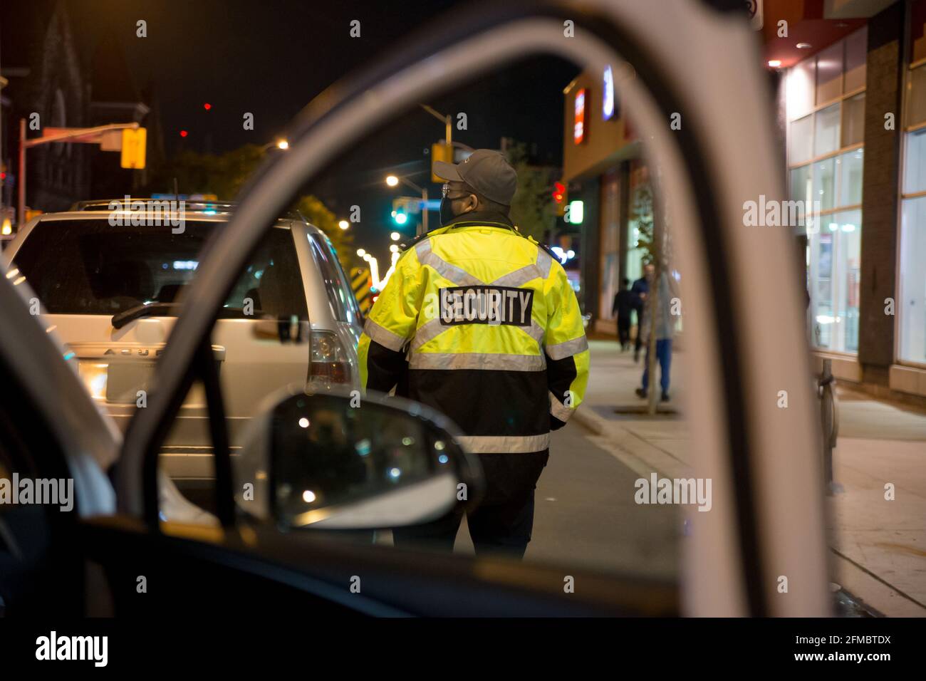 Security guard standing next to a patrol car in midnight street Stock