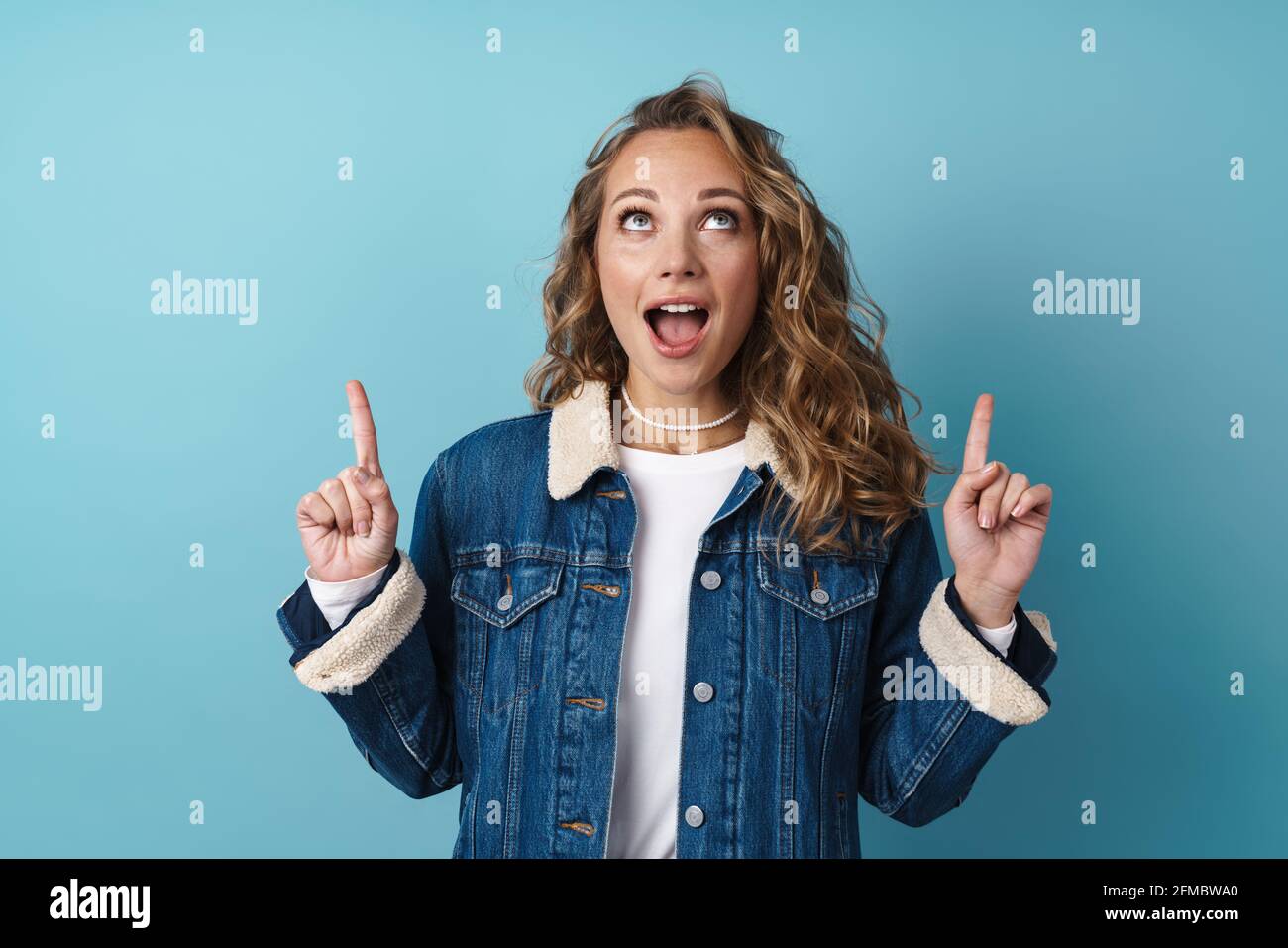 Blonde surprised woman looking and pointing fingers upward isolated ...