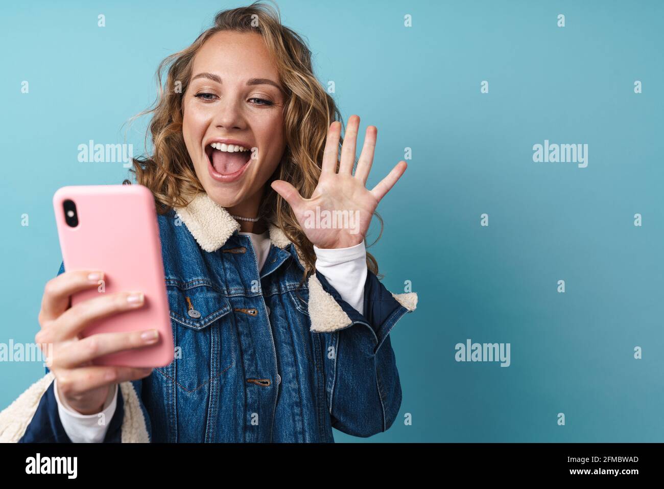 Blonde excited woman using mobile phone and gesturing isolated over blue wall Stock Photo