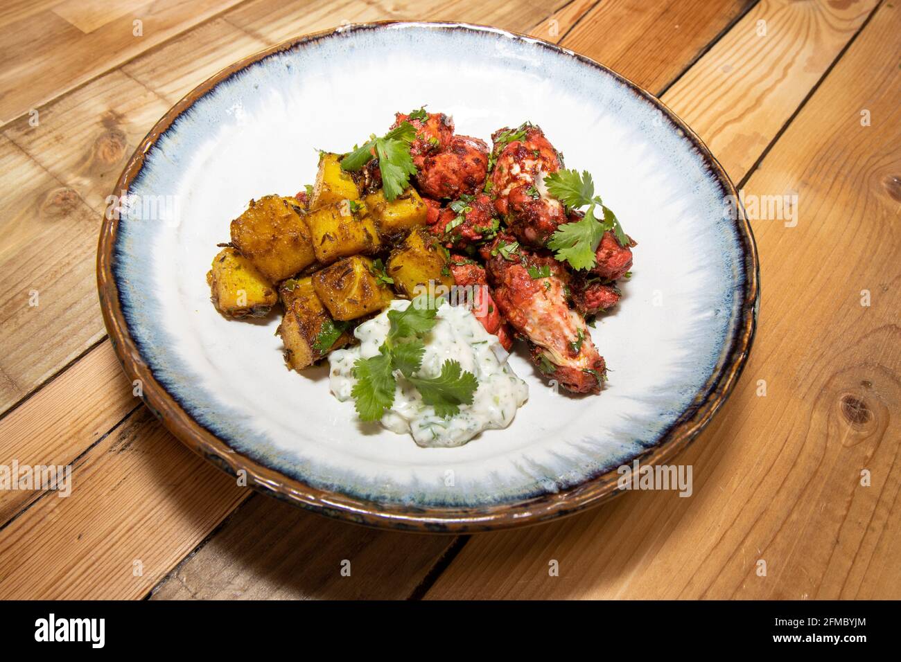 A plate of delicious Tandoori Chicken and cumin pan roasted potatoes on a wooden kitchen table Stock Photo